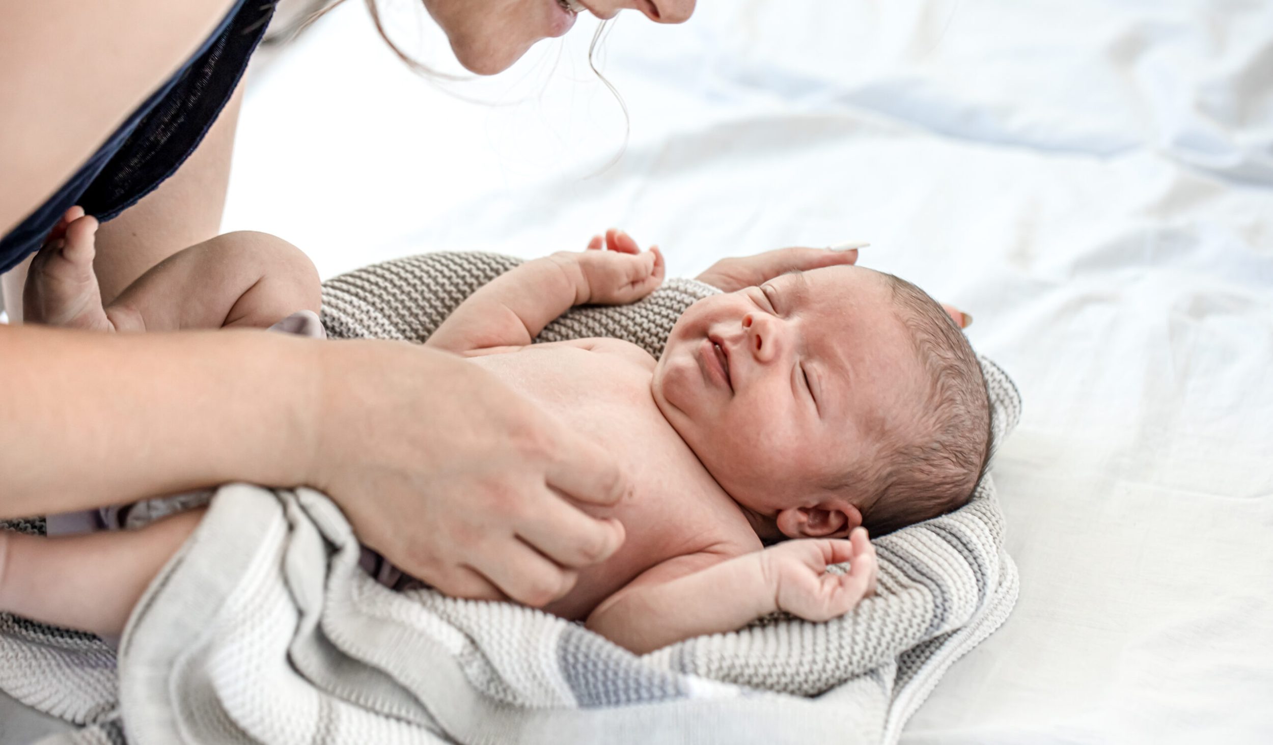 Mom talks and laughs with her newborn son at home bedroom.