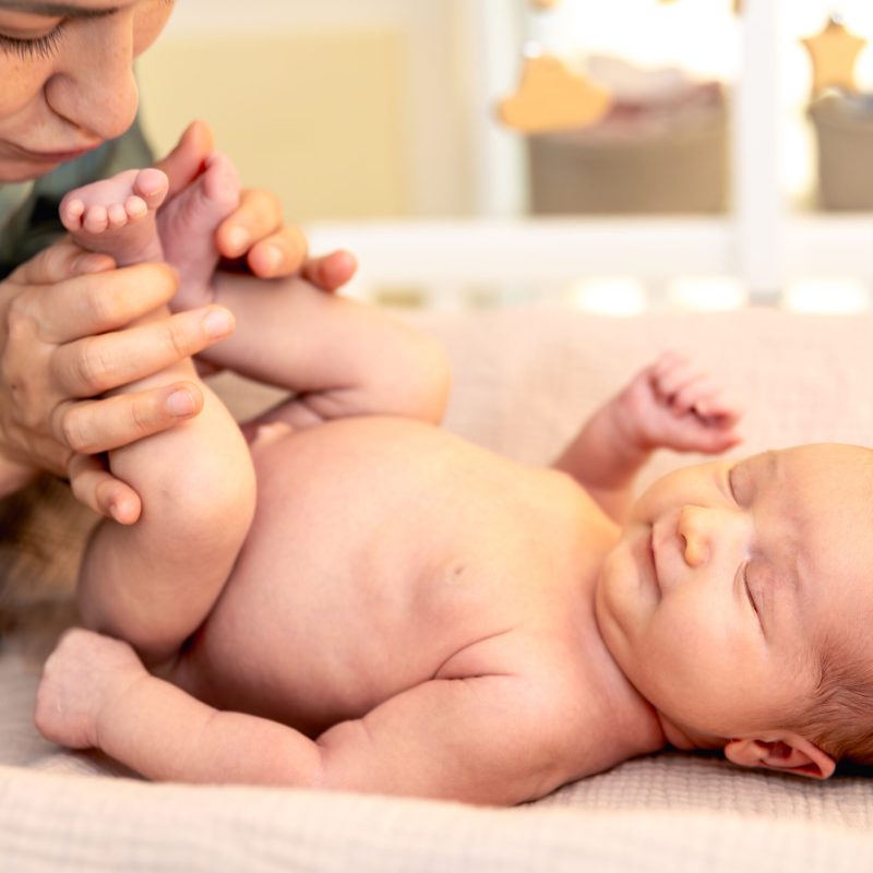 A young mother with a newborn baby. Newborn baby. High quality photo. Mother kissing baby daughter lying on bed at home.