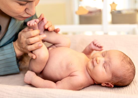 A young mother with a newborn baby. Newborn baby. High quality photo. Mother kissing baby daughter lying on bed at home.