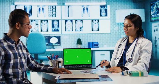 Woman doctor meeting with a patient in medical cabinet next to copy space on screen, employing technology at the hospital. Specialist medic helping a person with illness at check up. Camera B.